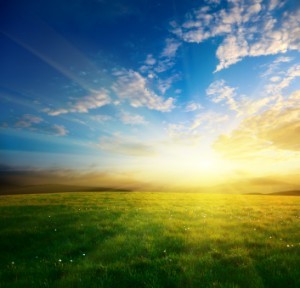 Sun rising over green field through a blue sky and clouds