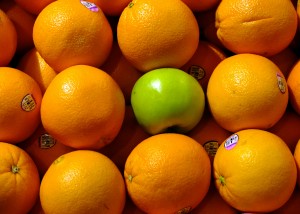 Rows of oranges with a green apple featured in the center