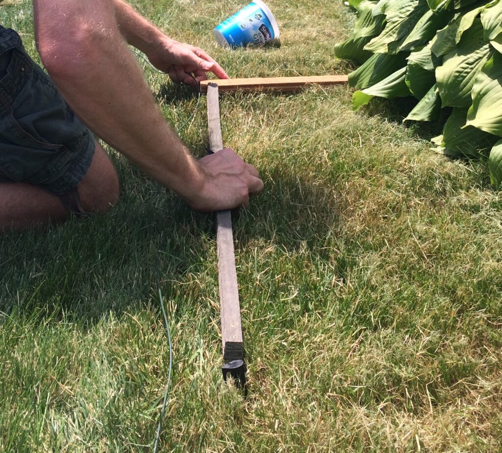 Shows a person's arms positioning the measuring tool on the grass with the wire aligned and one stake int he foreground.