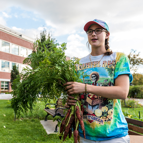 UVM student showing off carrots picked from a garden