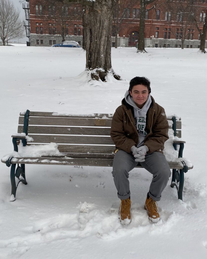 A person sitting on a wooden bench  with white snow around it.