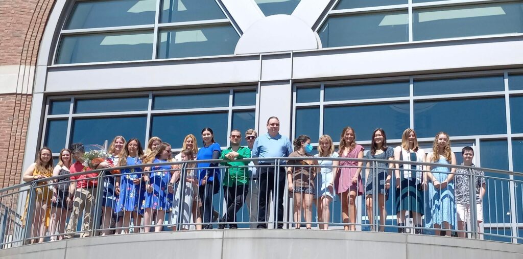 people standing on a balcony in front a large window.