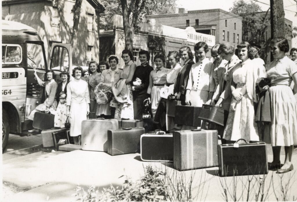 A group of young women with suitcases get ready to get on a bus.
