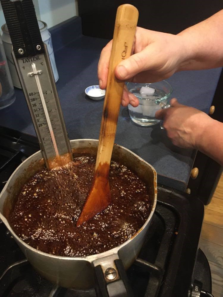 Cook stirs a pot on a stove holding the boiling molasses mixture and a thermometer.