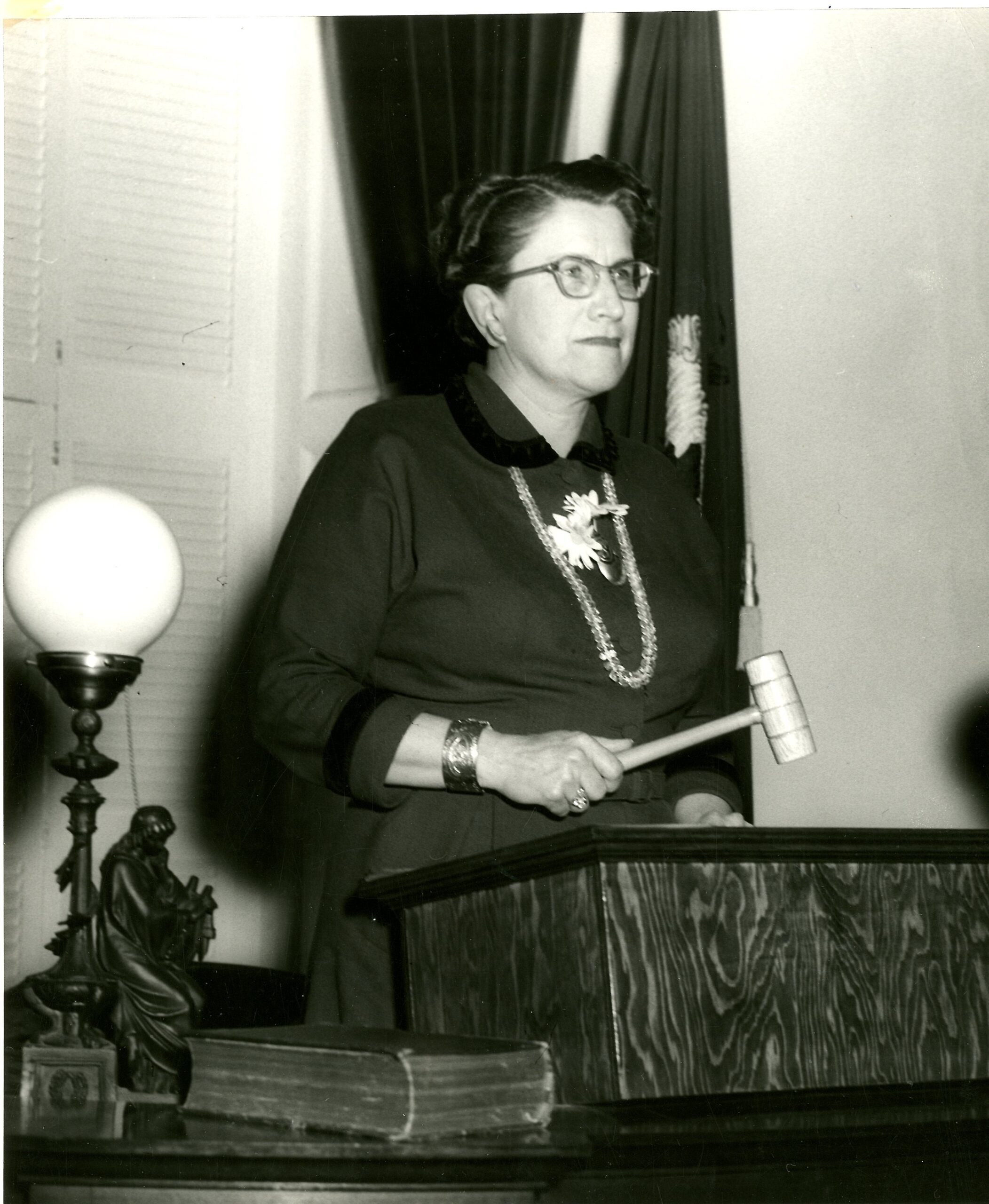 Consuelo standing at a podium holding a wooden gavel.