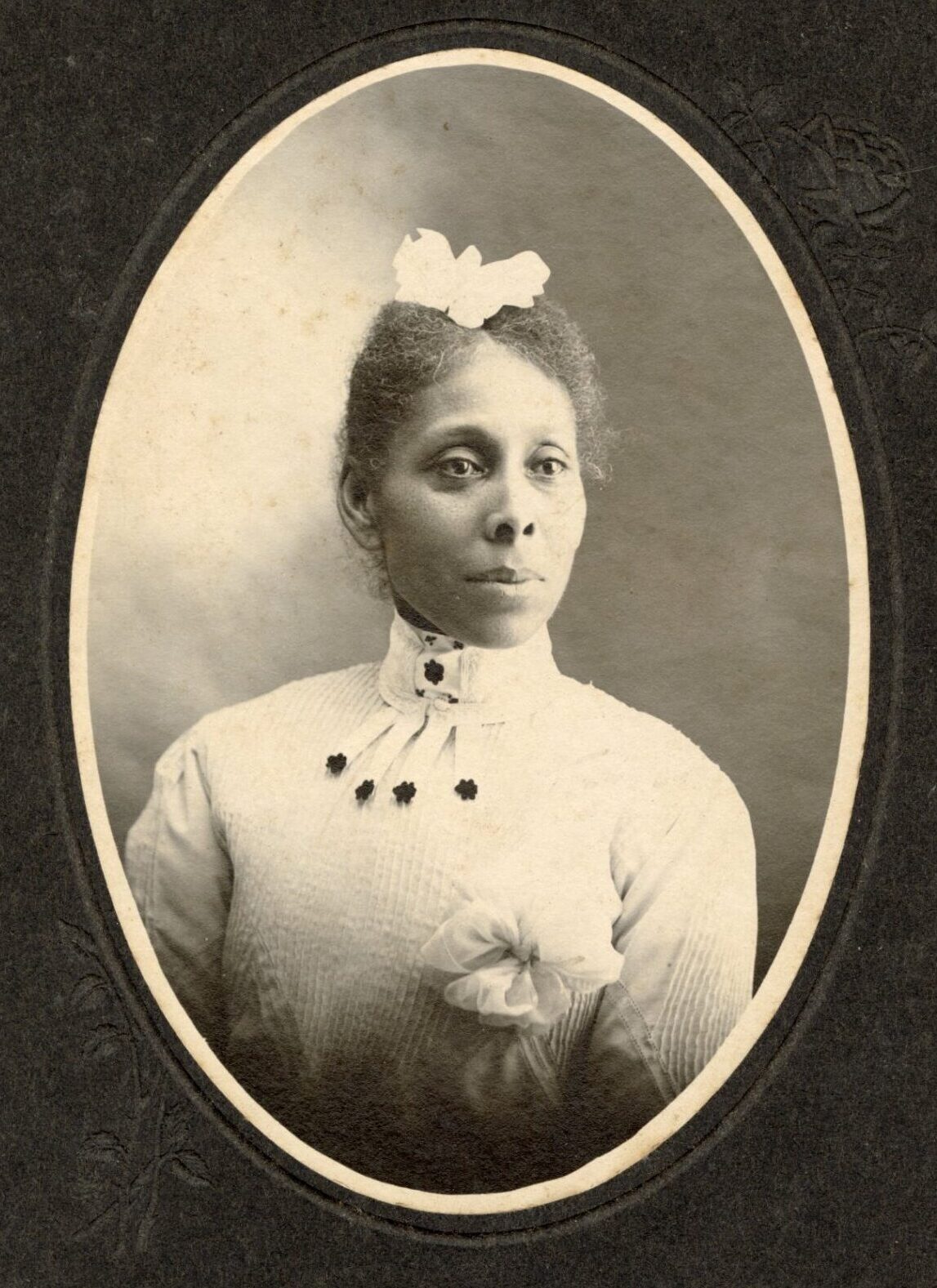 Studio portrait of Black woman wearing a fancy white blouse and a bow or hat on her head.