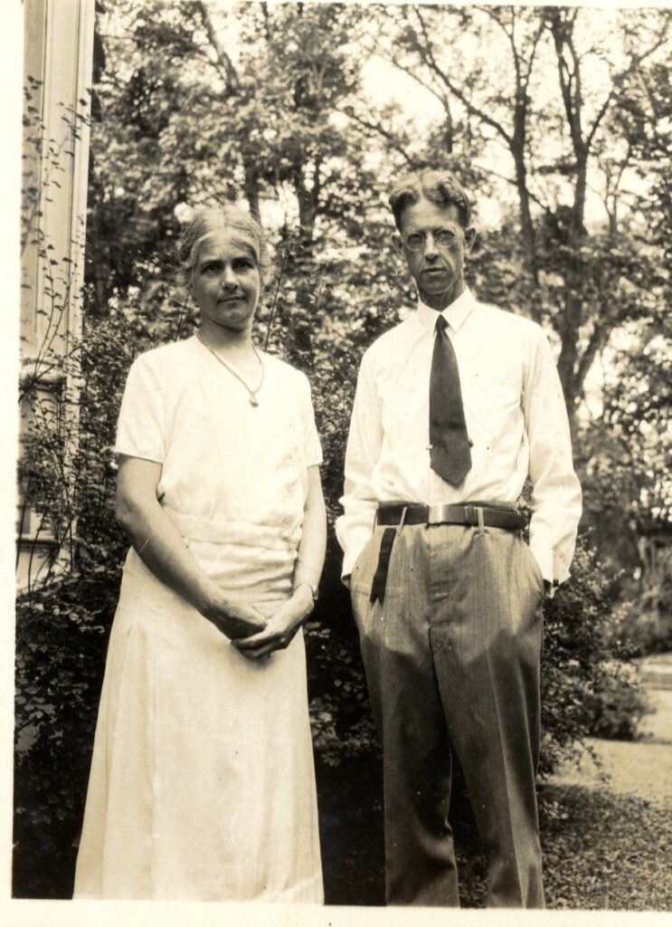 Jane Brownell in a light colored dress stands next to her husband Henry who is wearing a shirt and tiee.