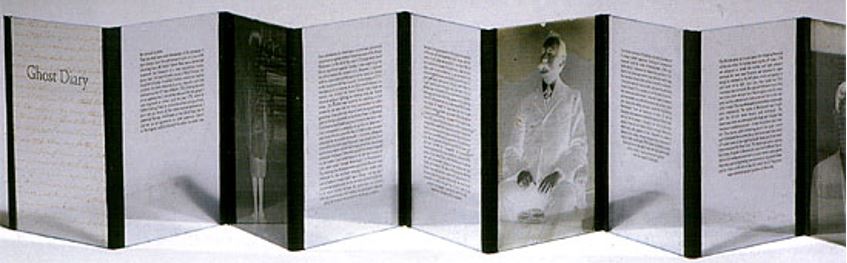 Image shows an open accordion book with text and photographs printed on glass panels joined with metal.