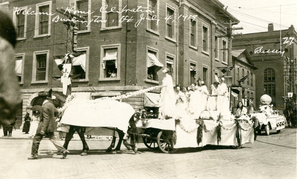 Women in white dresses ride on a horse-drawn parade float.t.