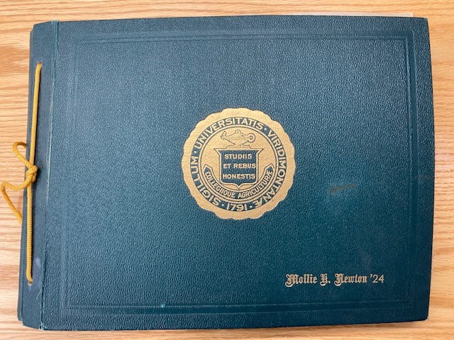Dark green cover of Mollie Newton's memory book bearing a gold UVM seal and laced with a yellow cord.