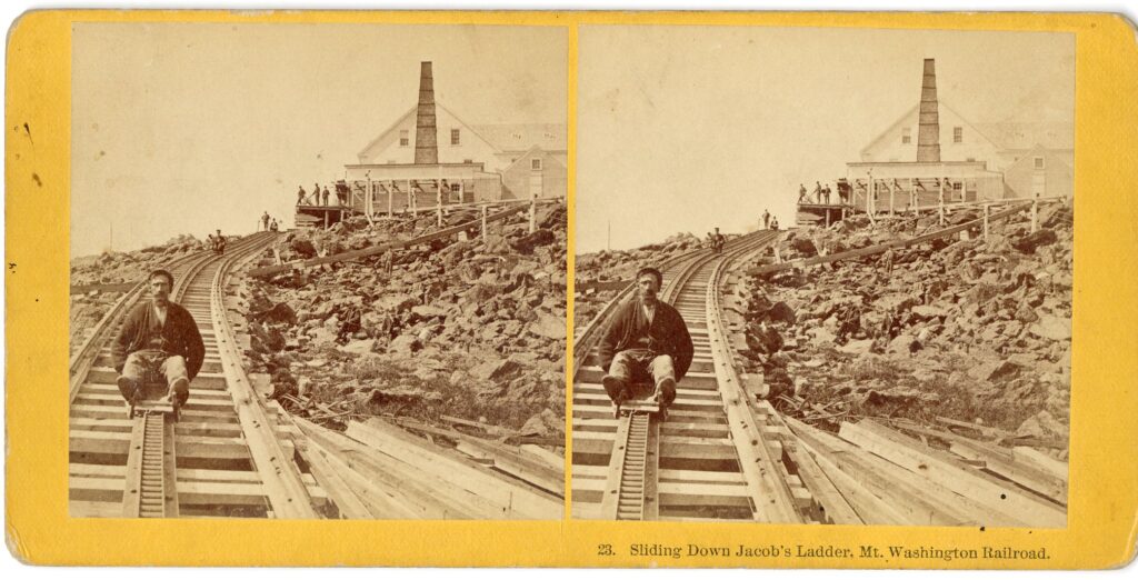 Two photographs mounted side by side on a yellow card showing a man seated on a board sliding down a cog railroad track.