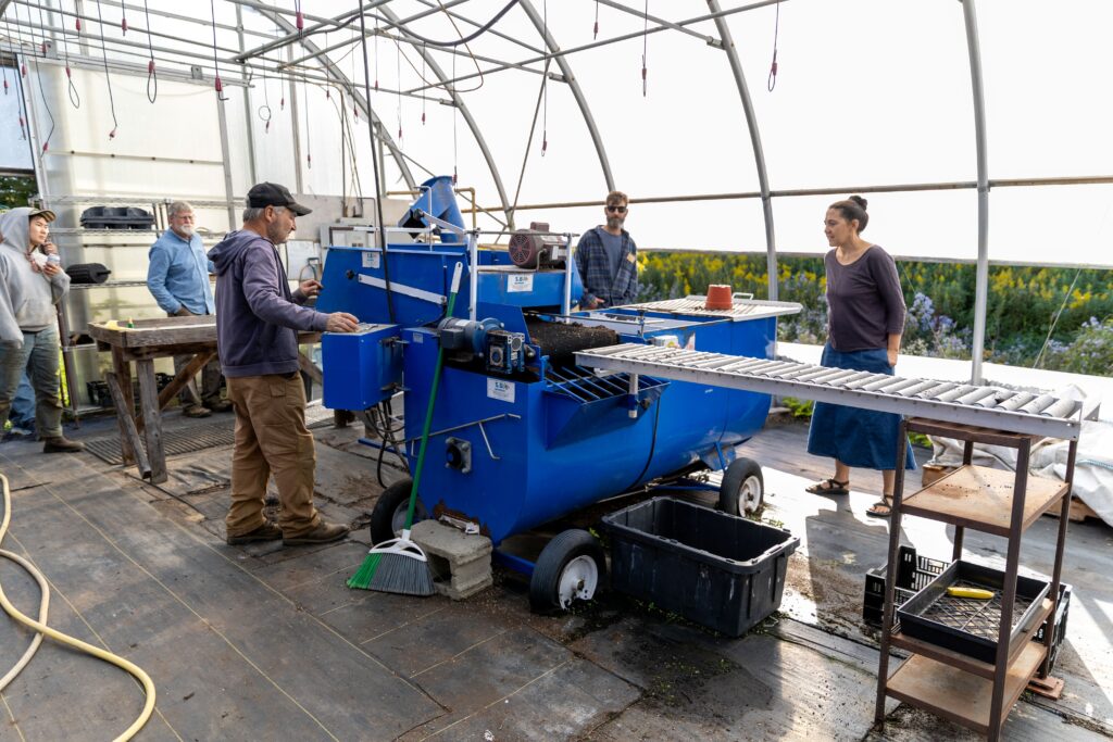 People gathered around equipment to fill flats with potting soil