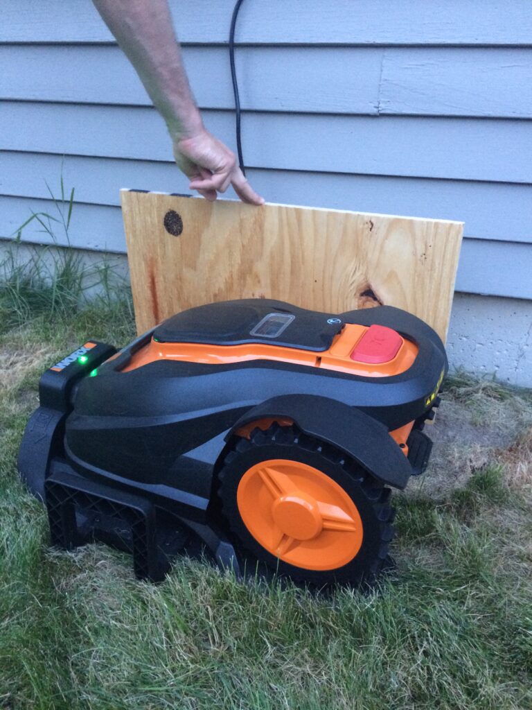 Sizing a board next to Mo the robotic mower to determine the height of the doghouse to be built for it.