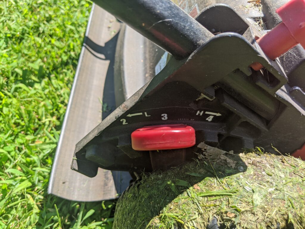 Close up of a gas-powered mower showing the lever and grass height selected based on where the lever is positioned. This mower is set at a 3" mowing height. 