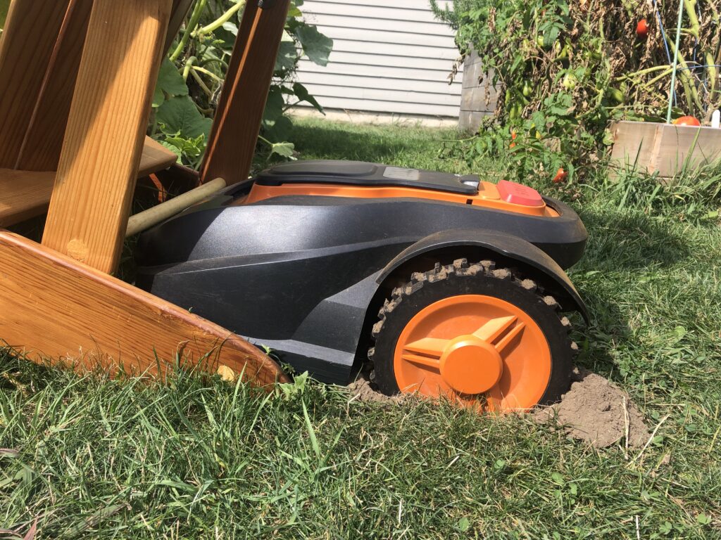 Mo the robotic mower stuck - again - in an Adirondack chair, with his wheels dug into the ground and dirt kicked up behind the wheels.