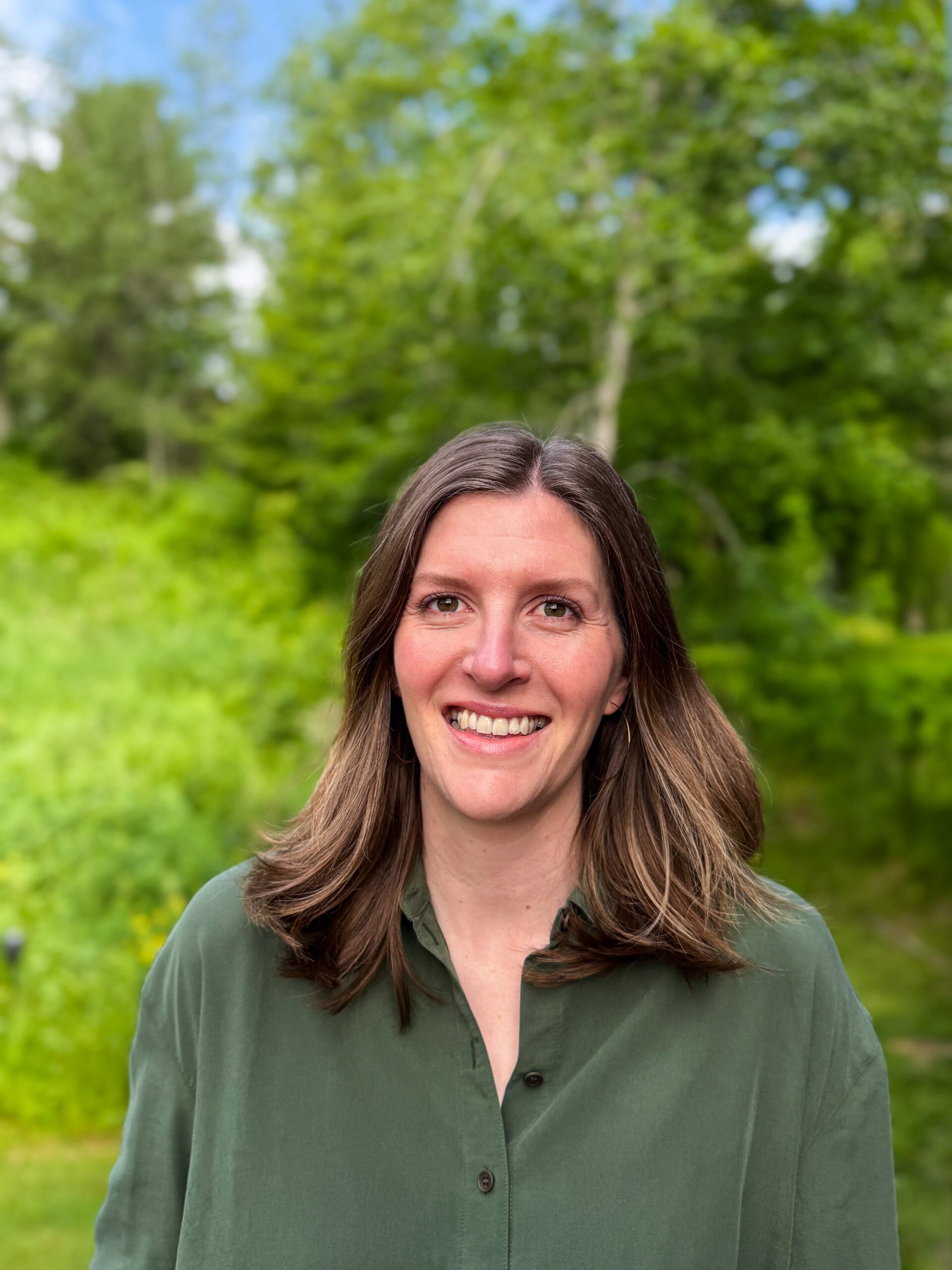 Photograph of Alayna, she is smiling, wearing a green shirt, she has medium-length brown hair.